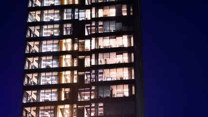 Modern office building in city center illuminated at night. Rows of lit windows against the architectural grid of a modern facade.
