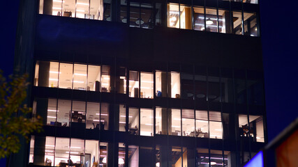 Modern office building in city center illuminated at night. Rows of lit windows against the architectural grid of a modern facade.