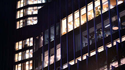 Modern office building in city center illuminated at night. Rows of lit windows against the architectural grid of a modern facade.