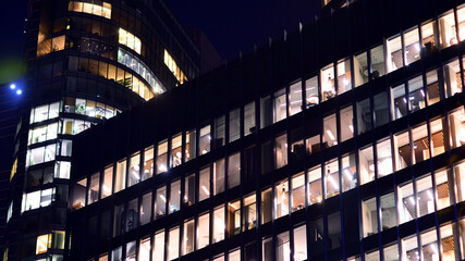 Modern office building in city center illuminated at night. Rows of lit windows against the architectural grid of a modern facade.