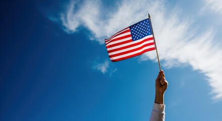 Hand Holding an American Flag Waving Proudly Against a Bright Blue Sky with Soft Clouds