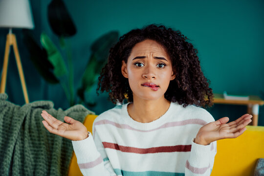 Confused woman on a colorful couch in a modern living room shrugging her shoulders and questioning daily choices