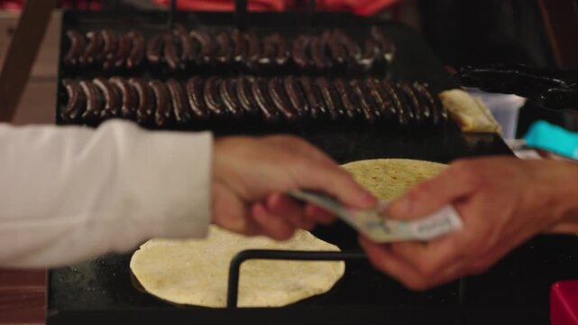 A blurry close-up of a customer paying a vendor for grilled sausages and arepas. This authentic scene depicts street food culture and commerce. Use for travel or food blogs.