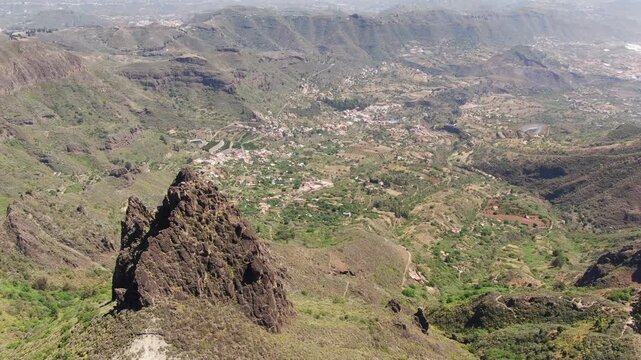 High aerial view revealing the lush green valley and mountains behind the Roque chico y Roque Grande in Gran Canaria
