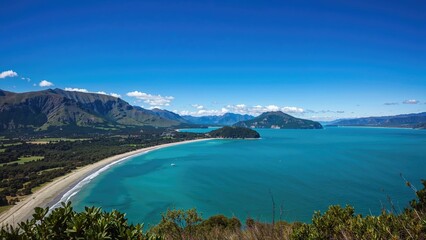 Fototapeta premium Scenic view of a beach with mountains in the background and a vibrant blue sky. Nature and landscape, coastal scenery, and outdoor adventure.