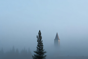silhouetted bell tower emerges through mist of winter morning creating ethereal atmosphere
