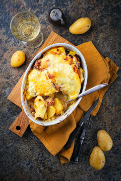 Artisan homemade oven baked Tartiflette wih potato and reblochon cheese in casserole dish served as top view on a wooden baord