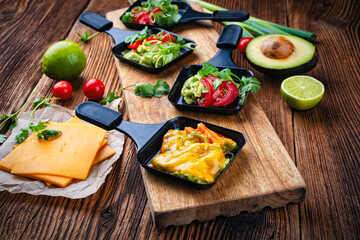 Vegetarian raclette with mached avocado, lime and cheddar cheese served as close-up on a wooden board