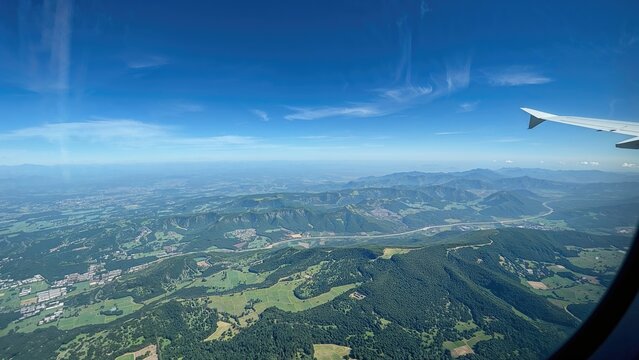 View of landscape from airplane window with rolling hills, forests, and sky visible.