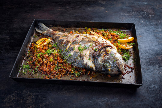Oven roasted saltwater whole gilthead sea bream with fried rice and vegetable mediterranean style recipe served as close-up on a plate
