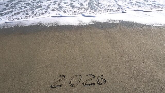 The inscription "2026" on the sand by the sea with a view of the horizon. The new year is 2026.