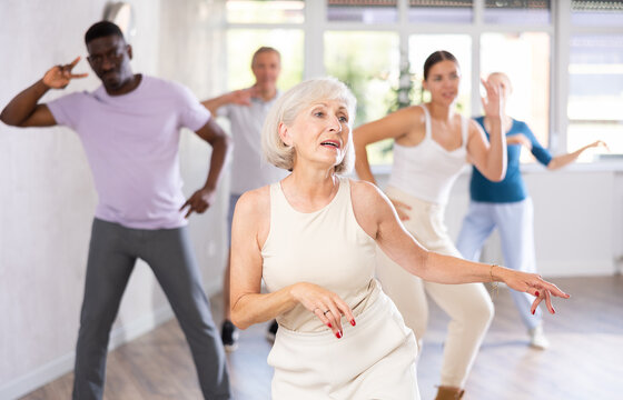 Young woman coach rehearsing with group of multinational sports aged people modern dance in dance hall