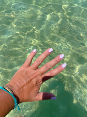 Sunbathing left woman hand with painted nails on a clear water beach background