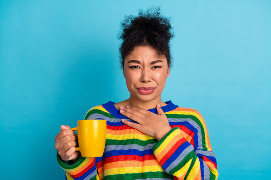 Young woman with rainbow striped sweater holding yellow mug against blue background smiling and expressing casual lifestyle advertising and fashion campaigns