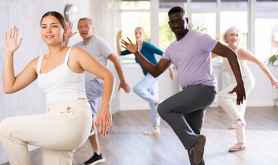 Young girl coach conducts classes for elderly in fitness studio. Female instructor teaches mature...