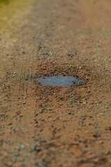 Small puddle on brown gravel dirt road.