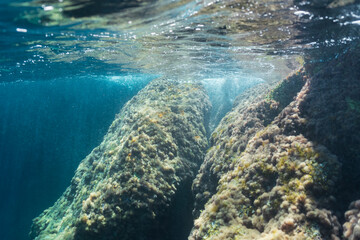 Obraz premium Sunlight illuminates a passage between large underwater rocks covered in algae, beneath the surface in Saint-Jean-Cap-Ferrat, France.