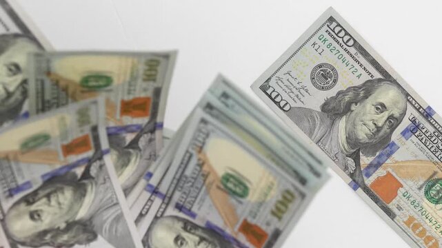 Hand holding multiple hundred-dollar bills, showcasing a gradual release of cash, with a focus on the vibrant details and textures of the currency