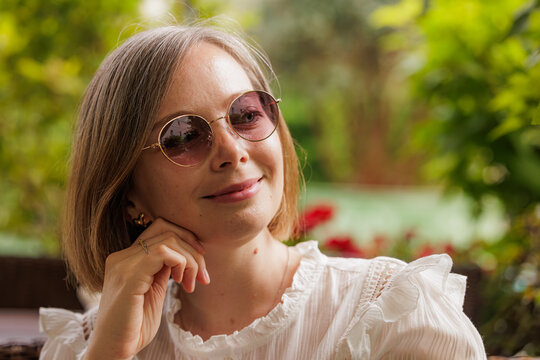 Smiling woman in stylish sunglasses enjoying a sunny day in a lush garden filled with vibrant flowers - Powered by Adobe