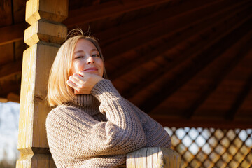 Smiling woman enjoying a sunny day in a wooden gazebo at a serene park during autumn