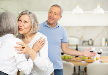 Fototapeta premium Two elderly women friends hugging in kitchen at home