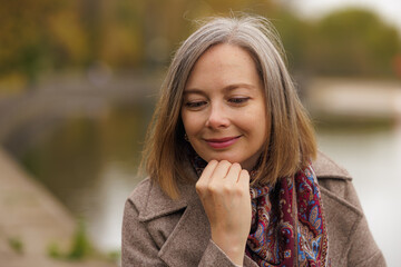Woman reflecting by the serene waters of a tranquil park in autumn
