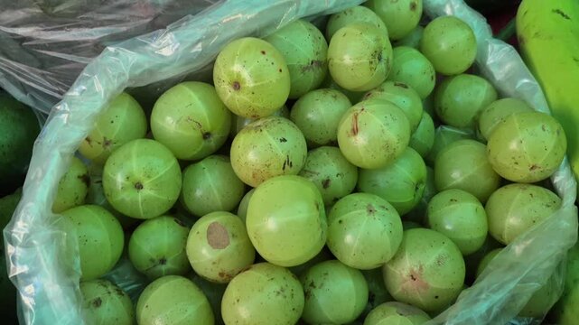 Indian gooseberries or amla fruits are arranged in a small bag pile for sale, showing glossy green surface.
