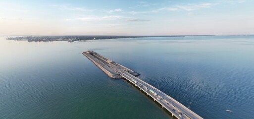 Aerial View Of Long Monitor Merrimac Memorial Bridge Tunnel crossing tranquil blue water of Hampton Roads Channel with a distant harbor and open sky
