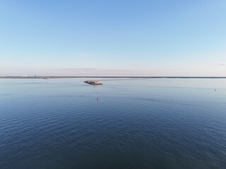 Aerial View Of Long Monitor Merrimac Memorial Bridge Tunnel crossing tranquil blue water of Hampton Roads Channel with a distant harbor and open sky