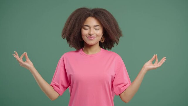 Tranquil woman relaxing, meditating, refuses stress. Young lady breathes deeply, calms down, green studio background. Yoga, moral balance, zen concept.