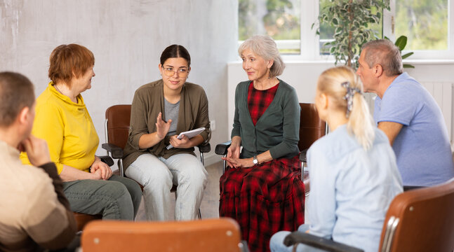 Emotional young female tutor leading educational class for group of older women and men..