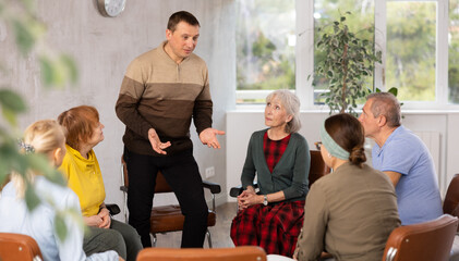 Portrait of positive adult man leading education class for group of elderly people, discussing interesting topics in classroom