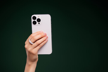 Woman hand holding a modern smartphone showcasing style, technology, and luxury against a rich green background