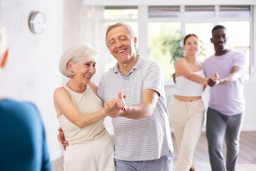 Active men and women of different ages practicing Ballroom dances in training hall during dancing...