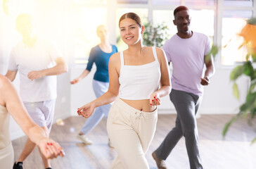 Fototapeta premium Young teacher and group of positive aged people engaged in dynamic dances in training room during workout session