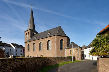 Historic European red brick church (St. Jakobus) with a slate steeple and clock tower, seen from a narrow street in Cologne Widdersdorf, Germany