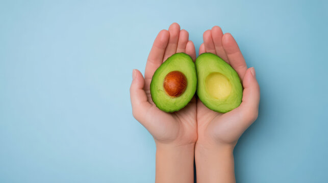 Fresh green avocado cut in half with seed held gently in two hands against soft blue background, symbolizing health and natural nutrition - Powered by Adobe