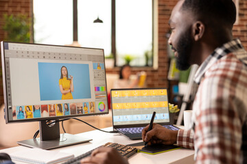 Black male illustrator using stylus and graphic tablet to create digital artwork from home. African american creative designer remotely edits and refines visual content in modern brick wall apartment.