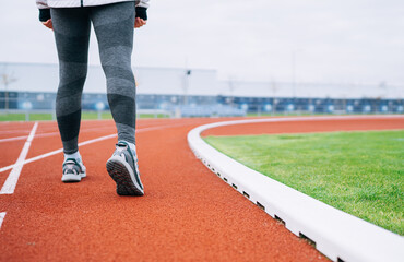 close-up photo of sporty female legs in running shoes ready for long walk or jog, healthy lifestyle, active women fitness and outdoor activity on Modern athletic stadium with red rubber running track