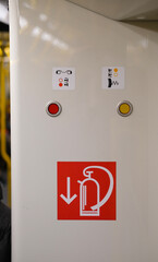 Emergency buttons and safety symbols on a light-colored panel, with a red “fire extinguisher” icon and arrow pointing downward.
