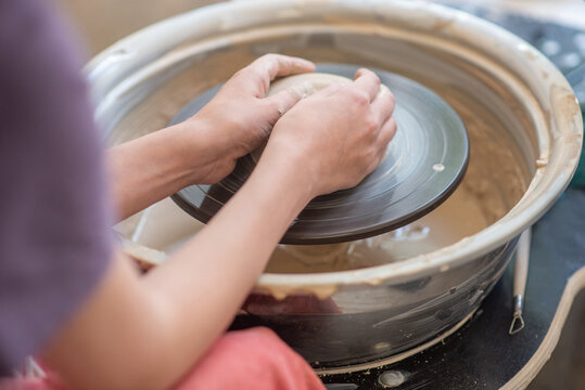 Close-up of a potter's hands centering a lump of wet clay on a spinning wheel. Focused, hands-on artistic process for craftsmanship, education, and ceramic art.