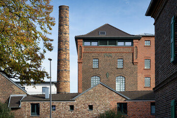 Preserved industrial red brick architecture (former SesterKoelsch  Brewery, 1904) with a prominent chimney, repurposed as modern residential housing in Cologne, Germany