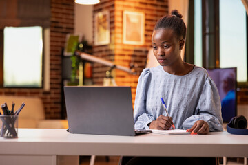 Hardworking female business owner reviews sales figures while seated indoors with laptop and...
