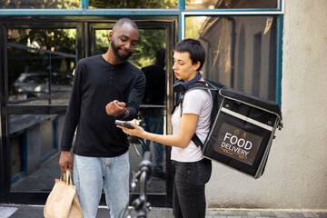 African American client paying with his smart watch at the pos, accepting a contactless payment from a customer. Electronic transaction finalizing the takeout delivery exchange.