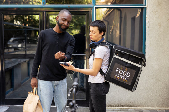 African American client paying with his smart watch at the pos, accepting a contactless payment from a customer. Electronic transaction finalizing the takeout delivery exchange.