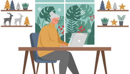 Happy senior woman using a laptop in a cozy home office decorated for winter holidays