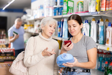 Young and mature women shopping in supermarket, chooses plastic bottle of household detergent