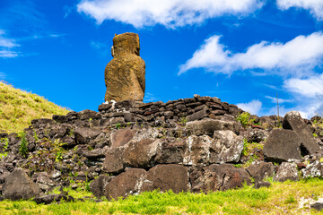 Low-angle view of the Moai statue on Ahu Ature at Anakena Beach, Easter Island. The lone stone ahu sits on a grassy hill under a blue sky with clouds