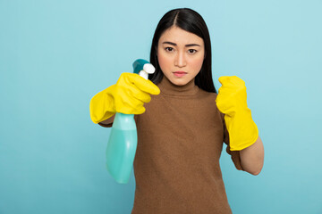 Female cleaner with rubber gloves stands in fight pose with spray bottle, expressing anger and stress from overwhelming household tasks. Frustrated asian woman ready to tackle messy chores.