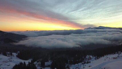 Aerial view of sunset over snowy mountains and clouds in winter